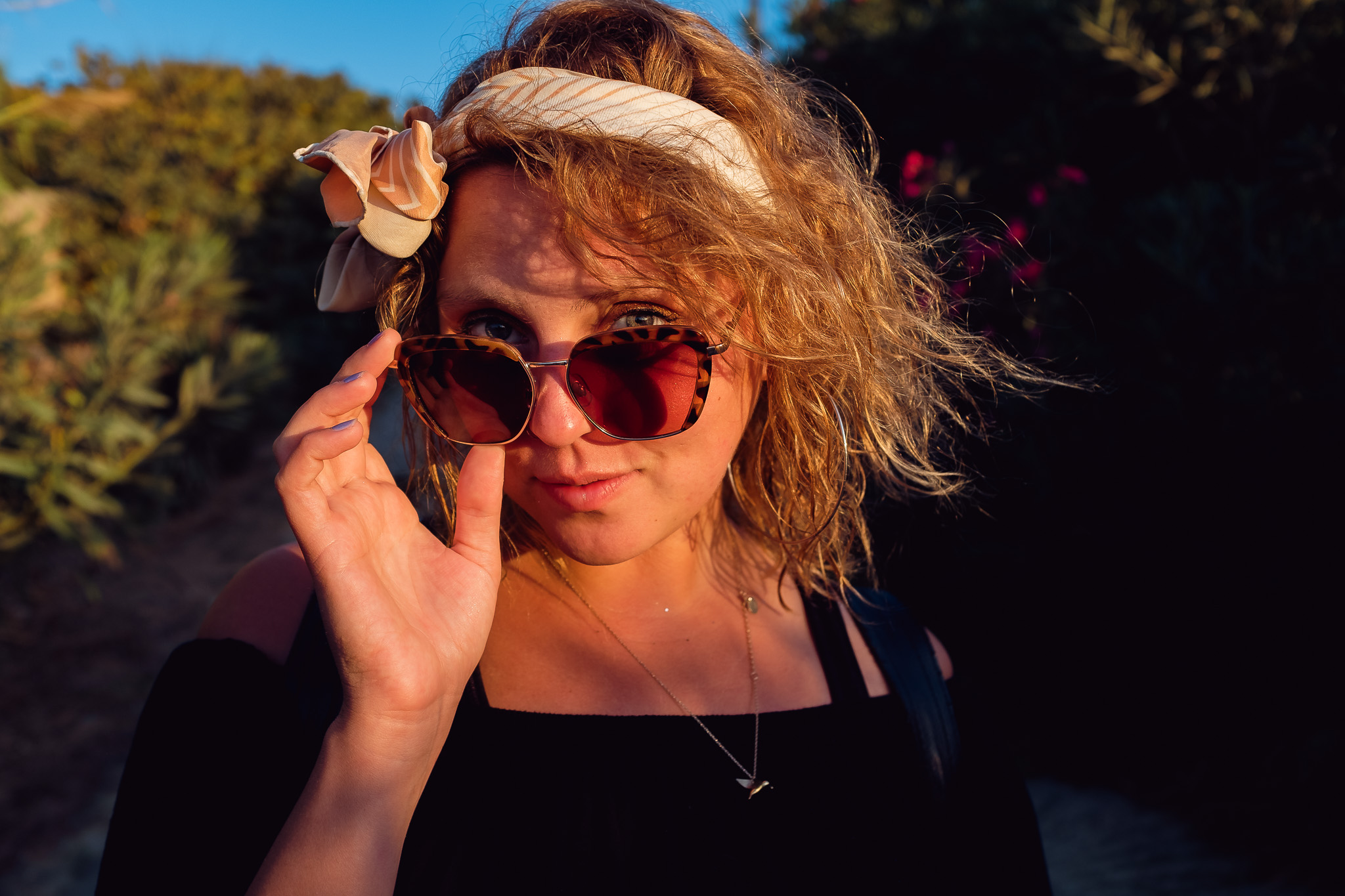 young woman holding her sunglasses and looking over them at golden hour