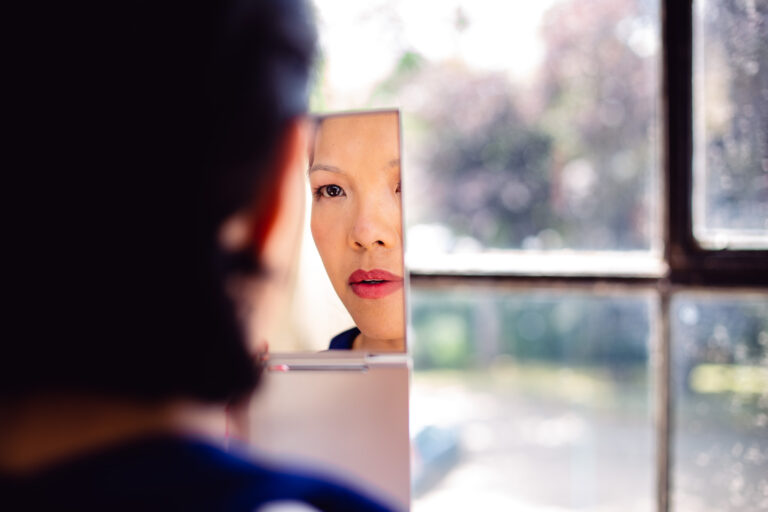 Brides looks at her reflection in a hand mirror getting her wedding makeup done.