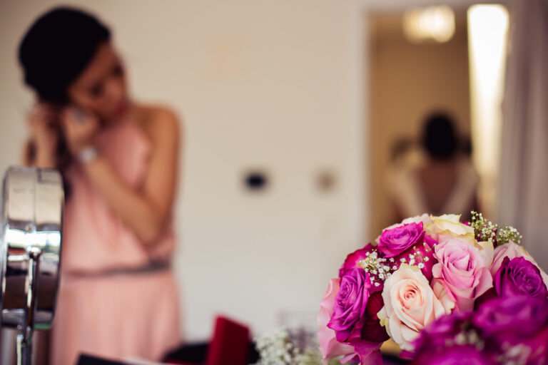 Bouquet of pink roses with bridesmaid in the background putting on earrings.