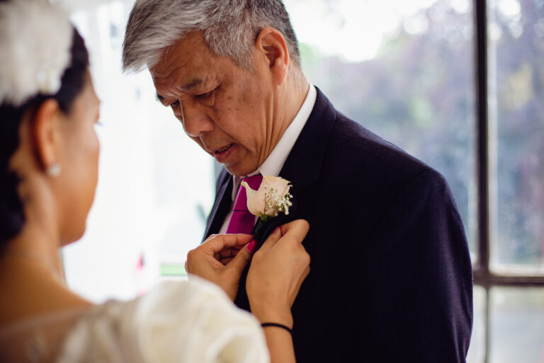 Bride attaching a buttonhole to her dad's jacket in preparation for her wedding day.