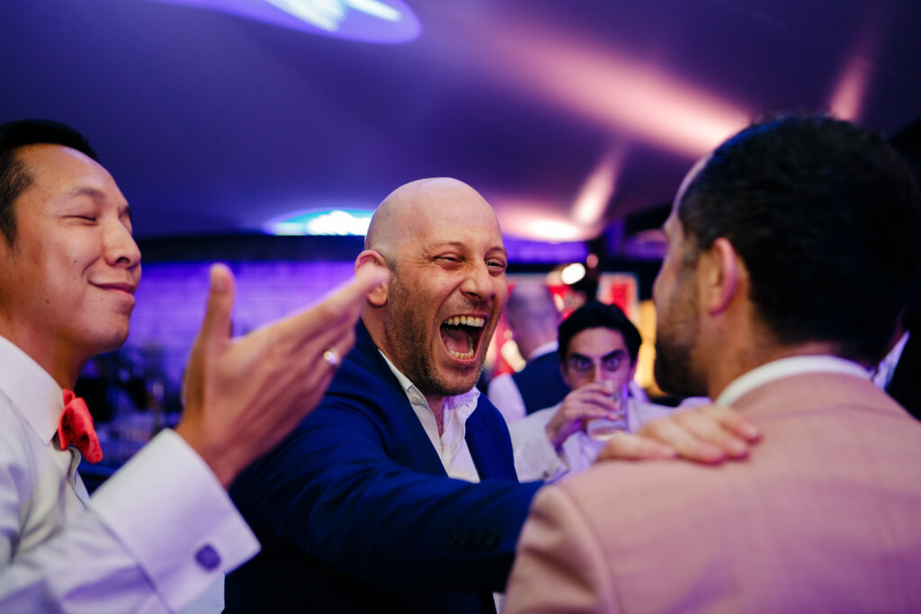 Men laughing and joking at a wedding reception in Thao Dien, Vietnam.
