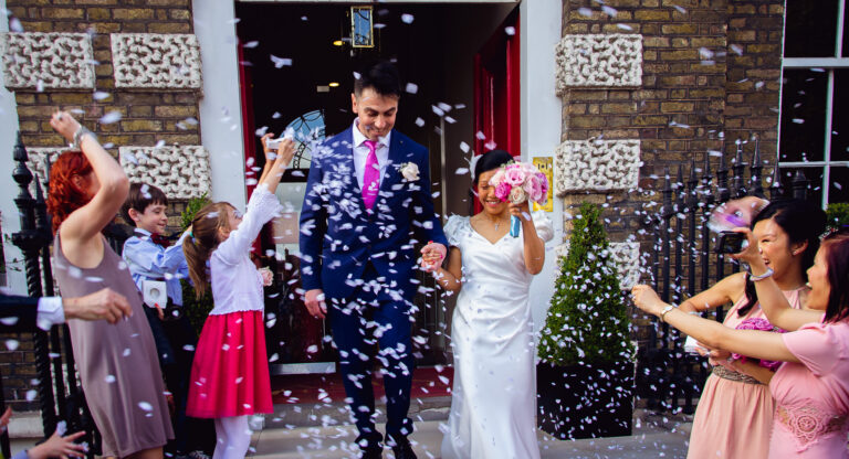 Bride and groom are just married and walking out of Asia House as guests throw confetti.