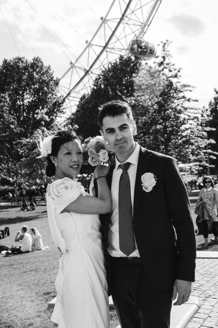 The bride and groom pose for a portrait in front of the London Eye.