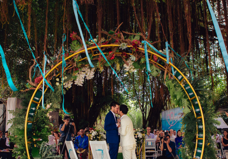 LGBTQ+ couple kissing in an arch under a tree canopy at their destination wedding in Vietnam.