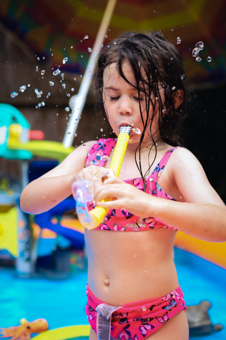 Summer children's portrait with a girl blowing water out of a snorkel in a paddling pool