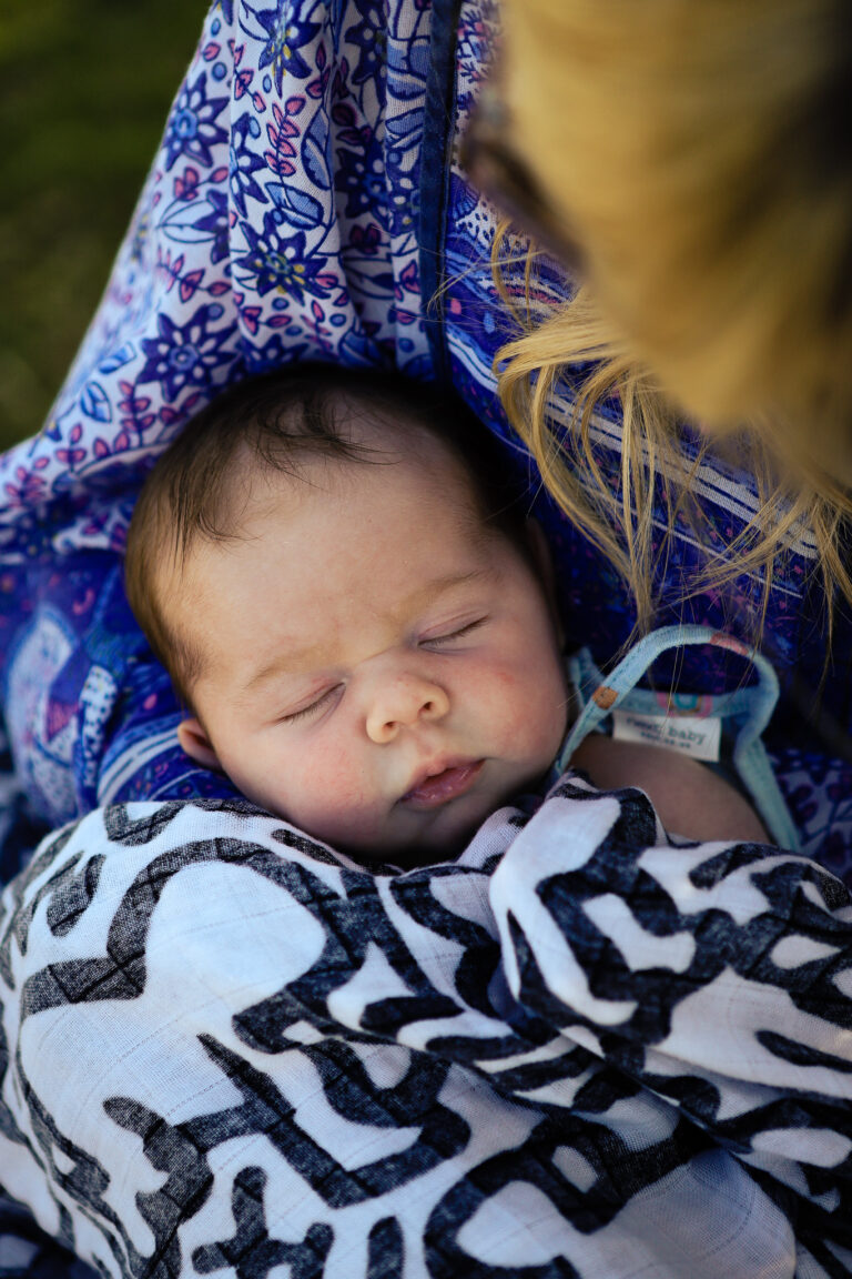 A sleeping baby covered by a Keith Haring baby blanket whilst held by her mum