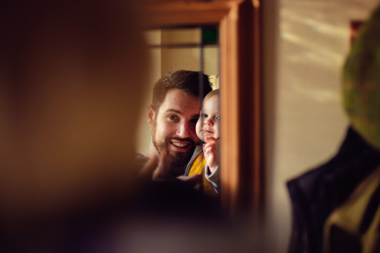 portrait of dad holding a toddler up to a mirror looking at their reflection