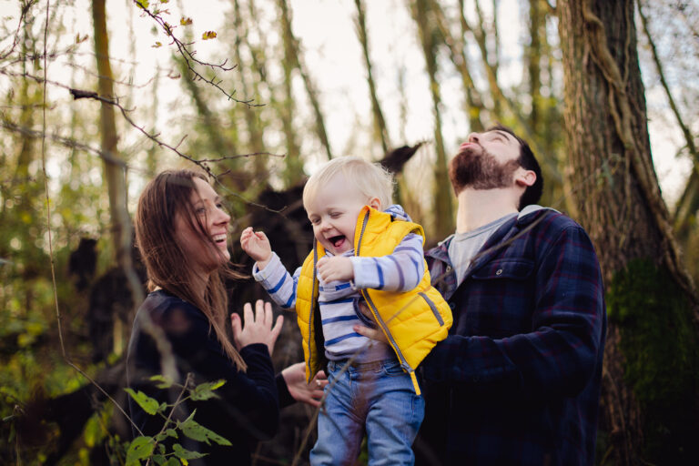 family portrait of laughing mum dad and toddler in a forest