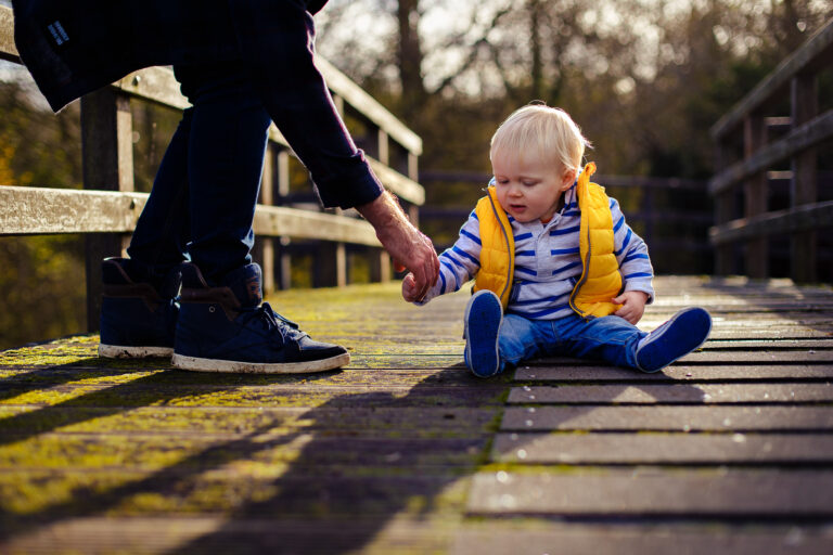 portrait of a toddler sitting on a bridge holding his dads hand