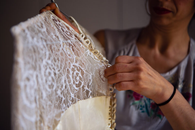 Bridesmaid undoing the buttons on the back of a vintage lace wedding dress.