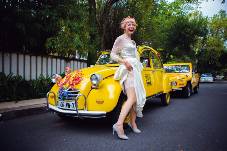 Bride laughing and showing her garter in front of two yellow cars just before heading to her wedding.