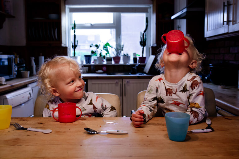Two young boy twins drinking milk at their kitchen counter during a family photo session
