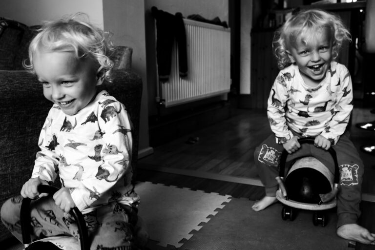 Two young boy twins laughing on little ladybird vehicles during a family photo session