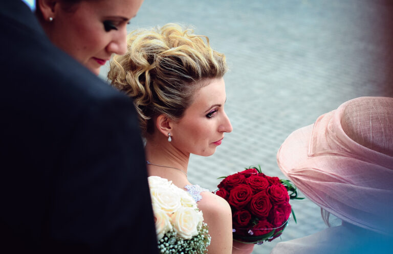 Bride looking over at the guests holding red roses during group wedding photo.