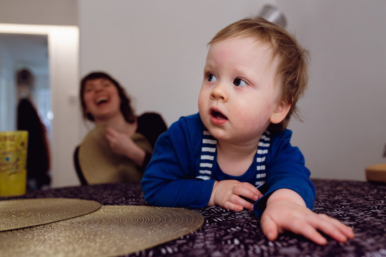 A toddler lying on table with mum laughing in the background during a family photo session