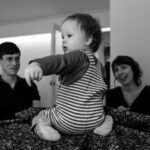 A toddler sitting on a table with mum and dad smiling in the background during a family photo session