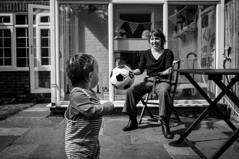 Mum throwing football to toddler in their garden during a family photo session