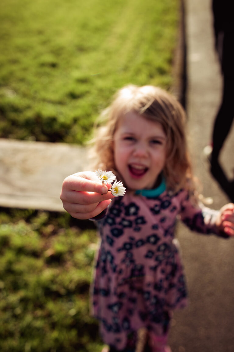 Rosa laughing and holding up two daisies while on a walk in the Irish countryside