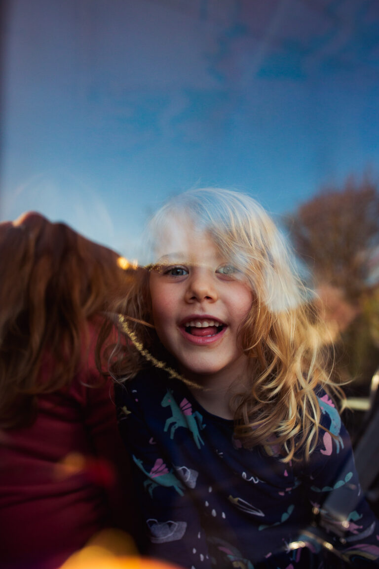 A smiling young girl in a unicorn dress through a window