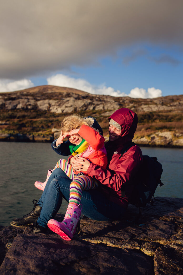 A mum and young girl sitting on the Irish coast on a windy winter day