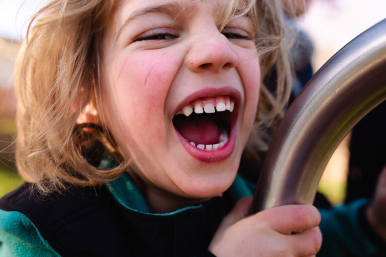 A young boy shouting and laughing with pen marks on his face on a climbing frame