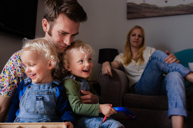 Mum sitting on a sofa with dad holding two young twin boys on his knees during a family photo session