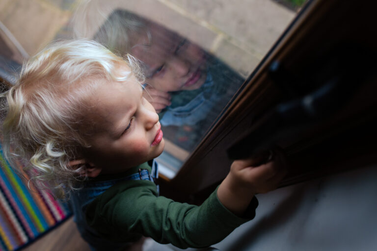 A young boy and his reflection in a window door trying to open the handle during a family photo session