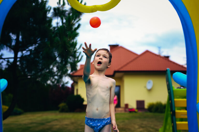 Kuba throwing a ball into a paddling ball hoop on a hot summers day in a garden in Poland
