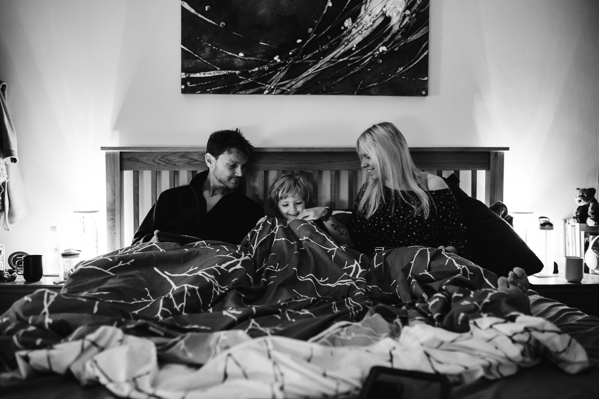 Mum, dad with their son in the middle watching an iPad in bed during a family photo session.