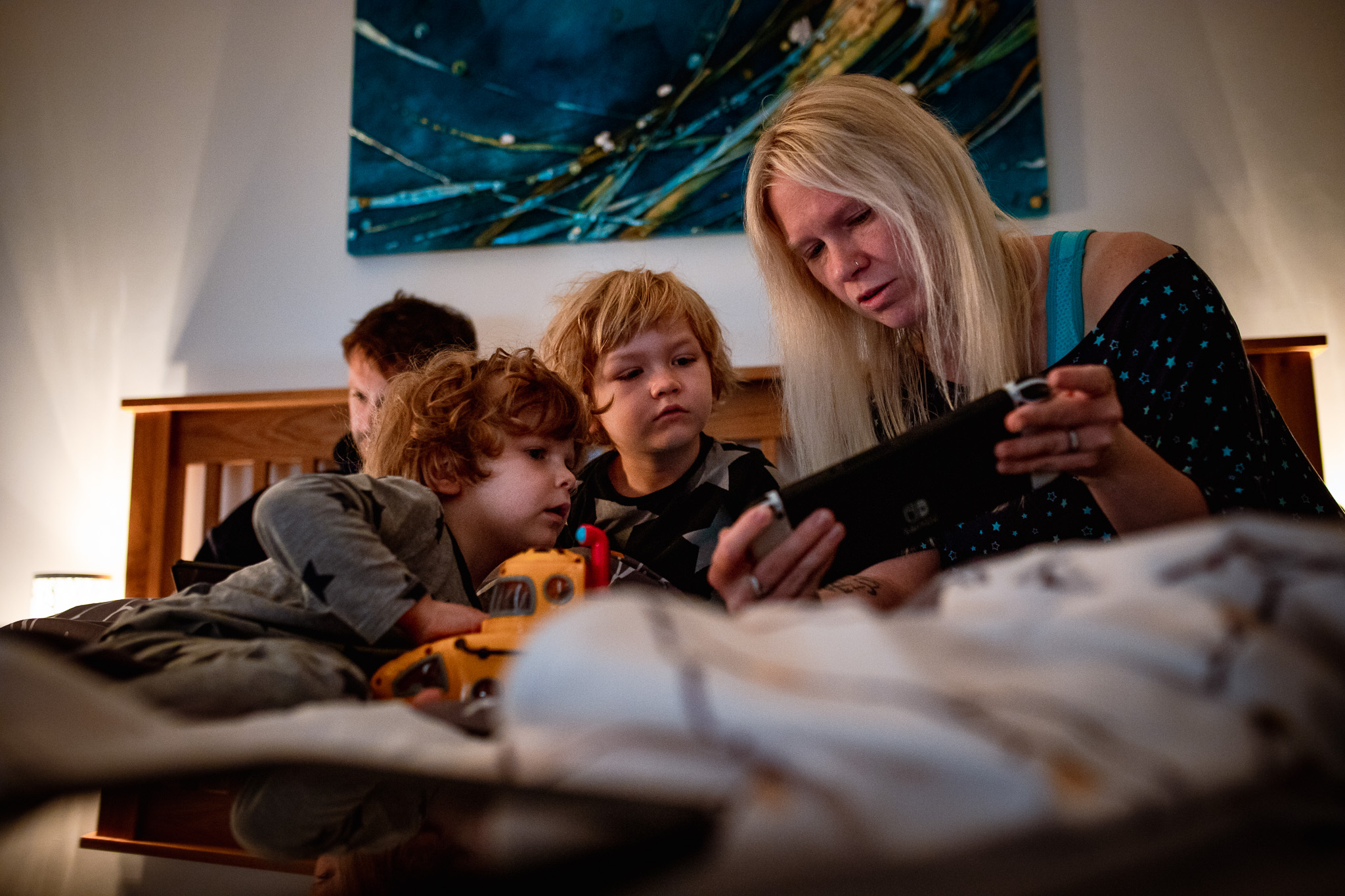 Family of four in bed with mum showing her two sons a Nintendo Switch during a family photo session.