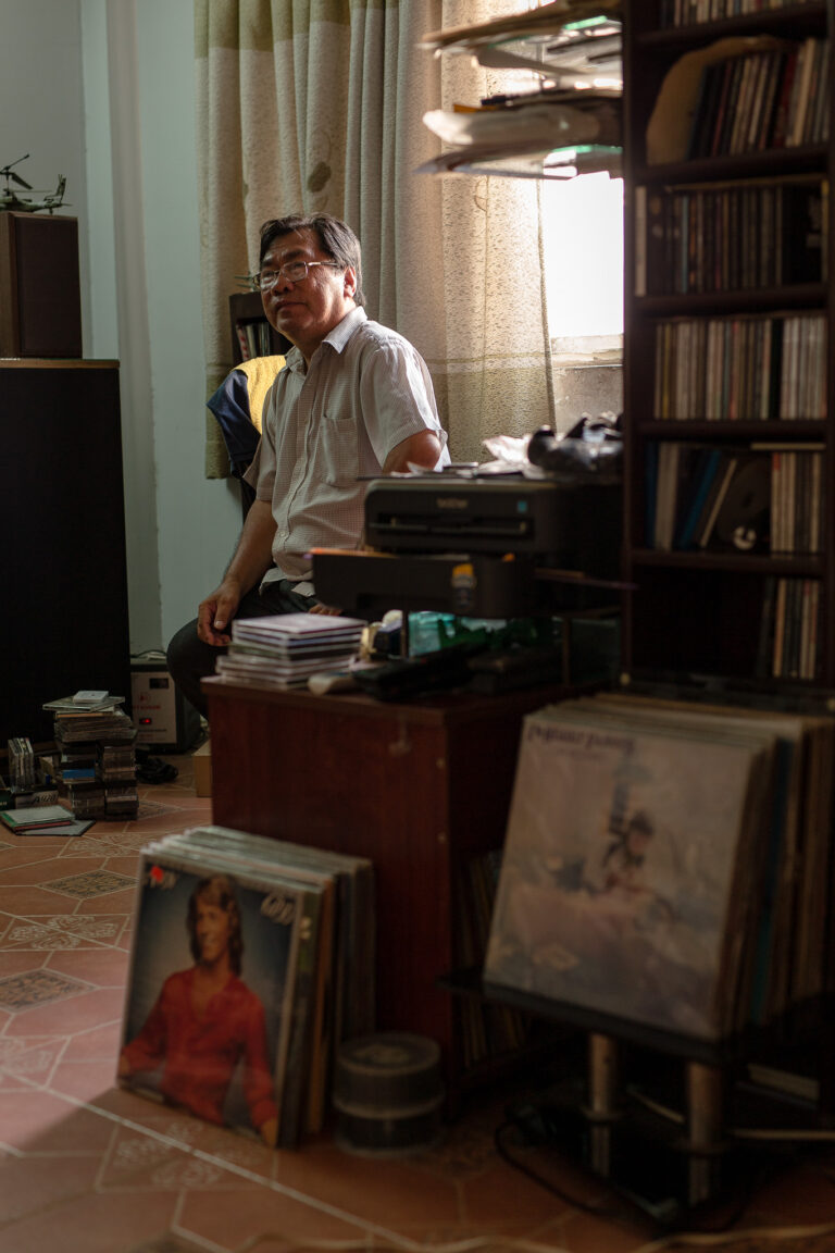 candid portrait of an older Vietnamese man surrounded by records and CDs