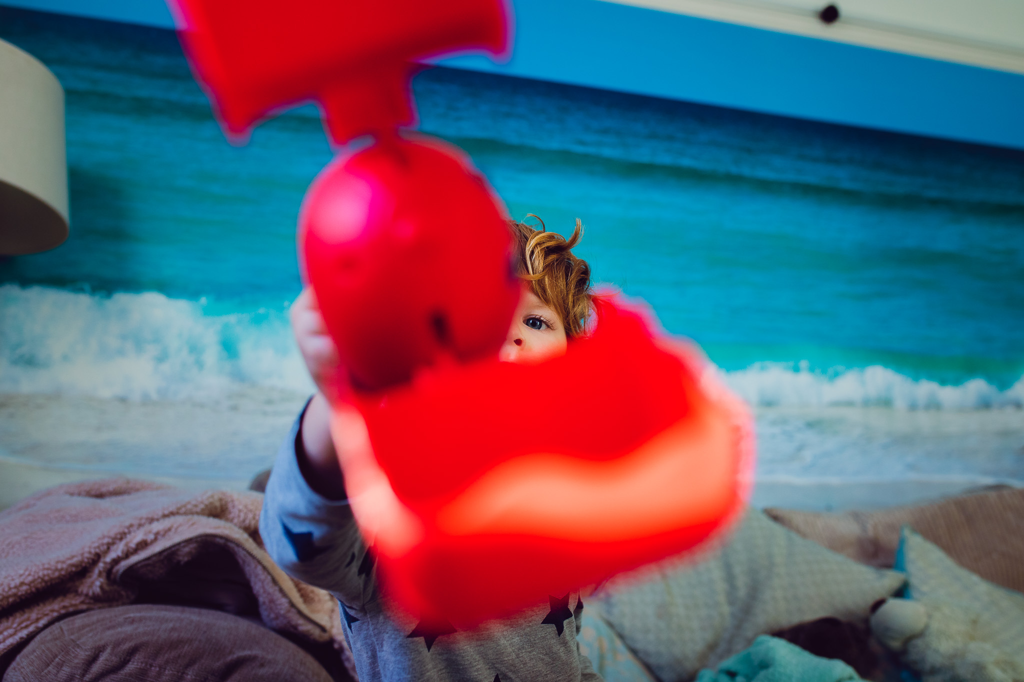 Leo is holding a red clamp toy forward, leaving only his eye visible during a family photo session.