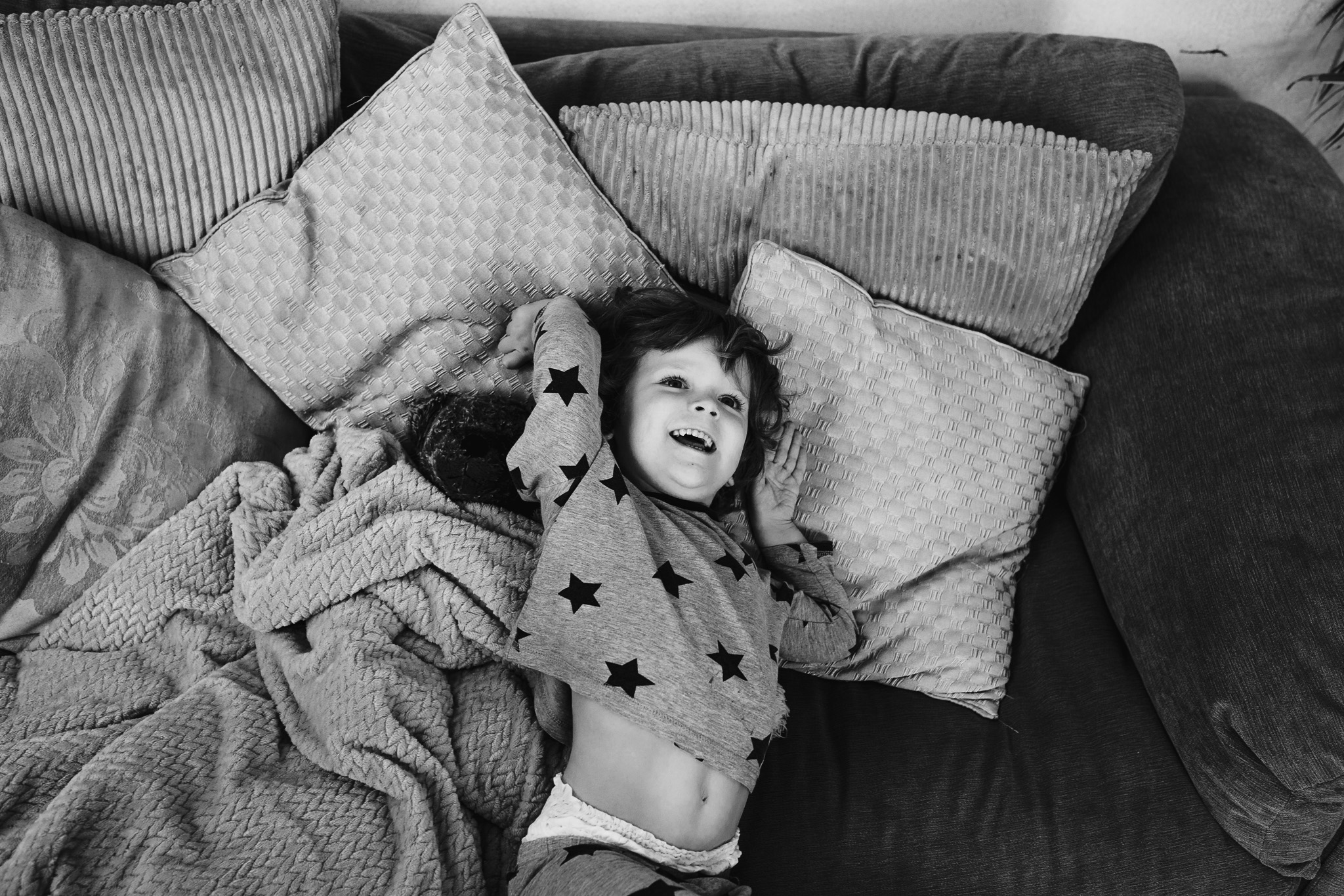 Young boy in star pyjamas laughing and playing on sofa cushions during a family photo session.