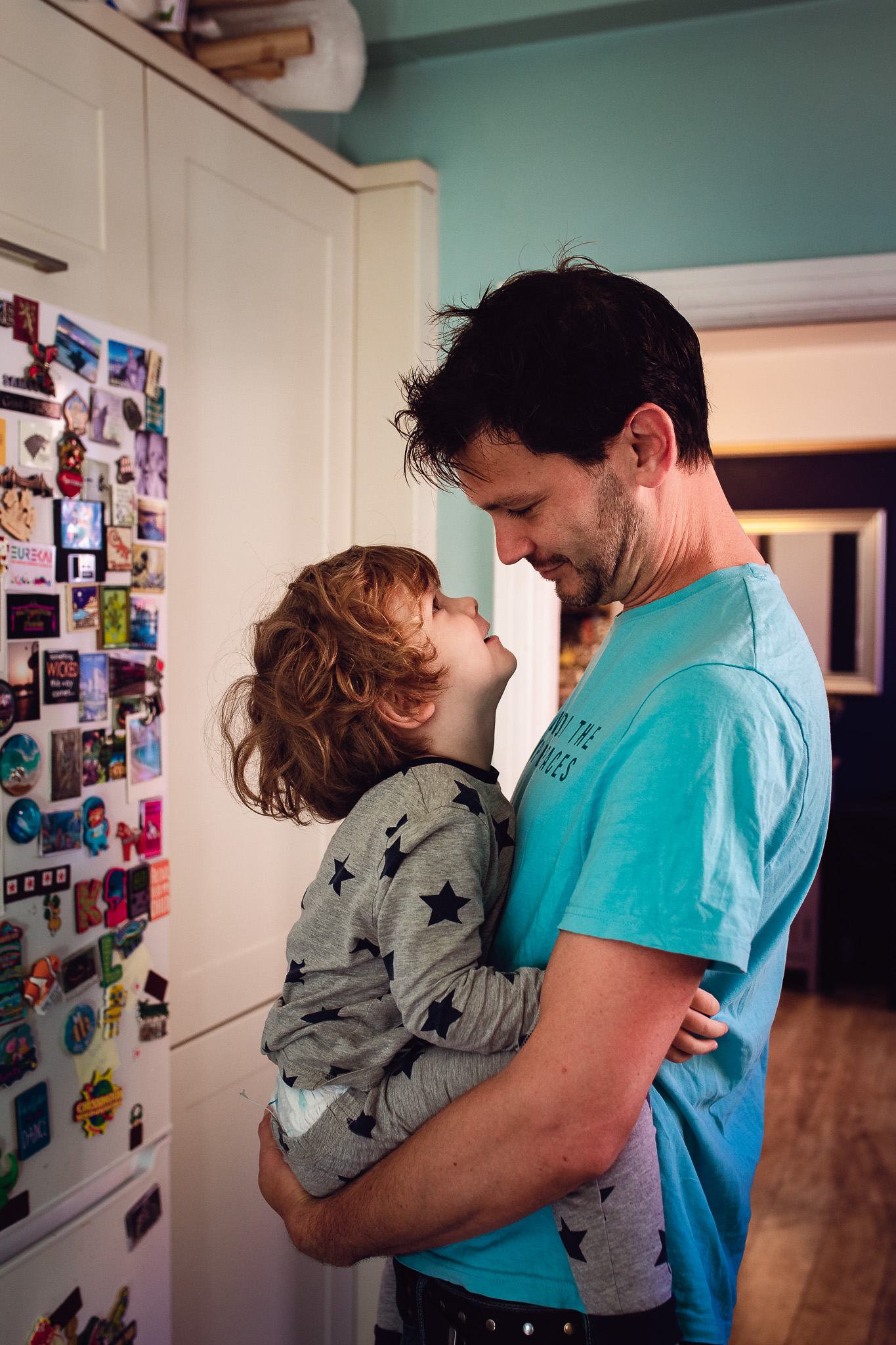 Dad and his young son are cuddling and looking at each other in the kitchen during a family photo session.