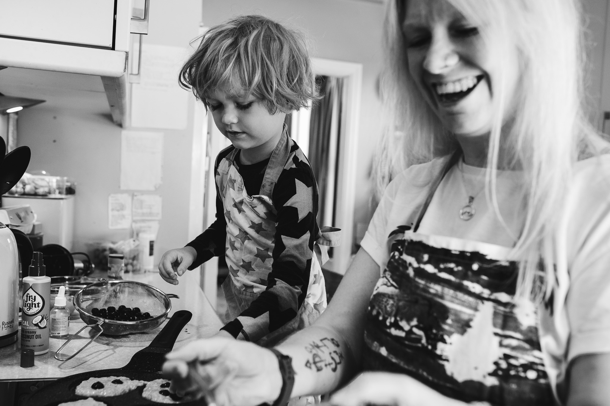 Young son and mum laughing and cooking pancakes together in the kitchen during a family photo session.