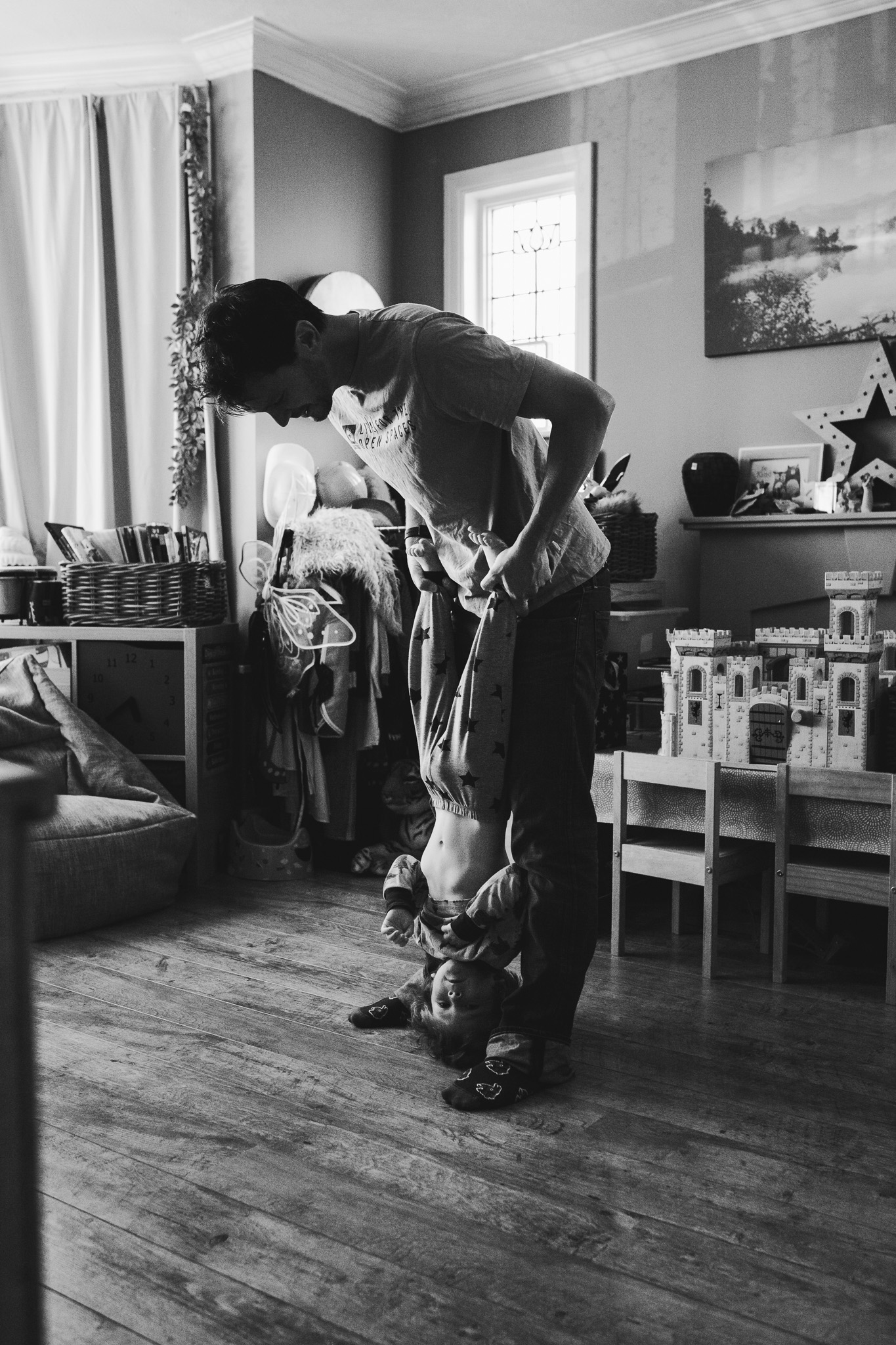 Dad is holding his son upside down in a playroom during a family photo session.