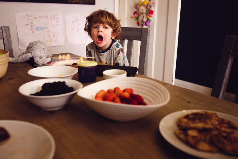 Young boy with an open mouth, waiting to eat pancakes at the table during a family photo session.