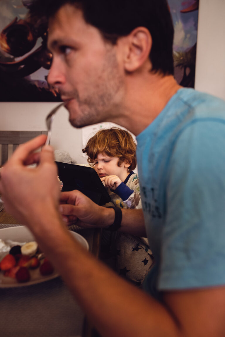 Young boy playing on an iPad while dad is eating during a family photo session.