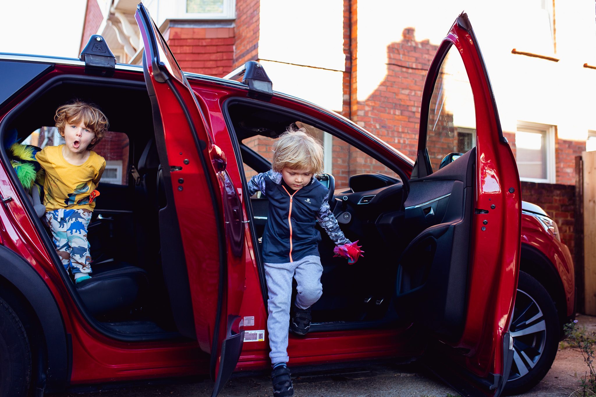 Two young boys jumping out of a red car during a family photo session
