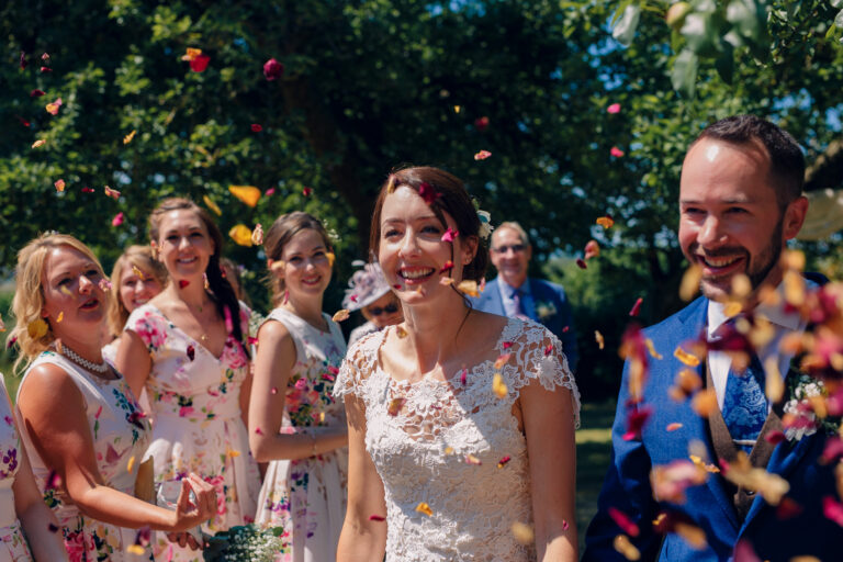 Bride and groom at wedding ceremony walking down the aisle with guests throwing flower confetti.