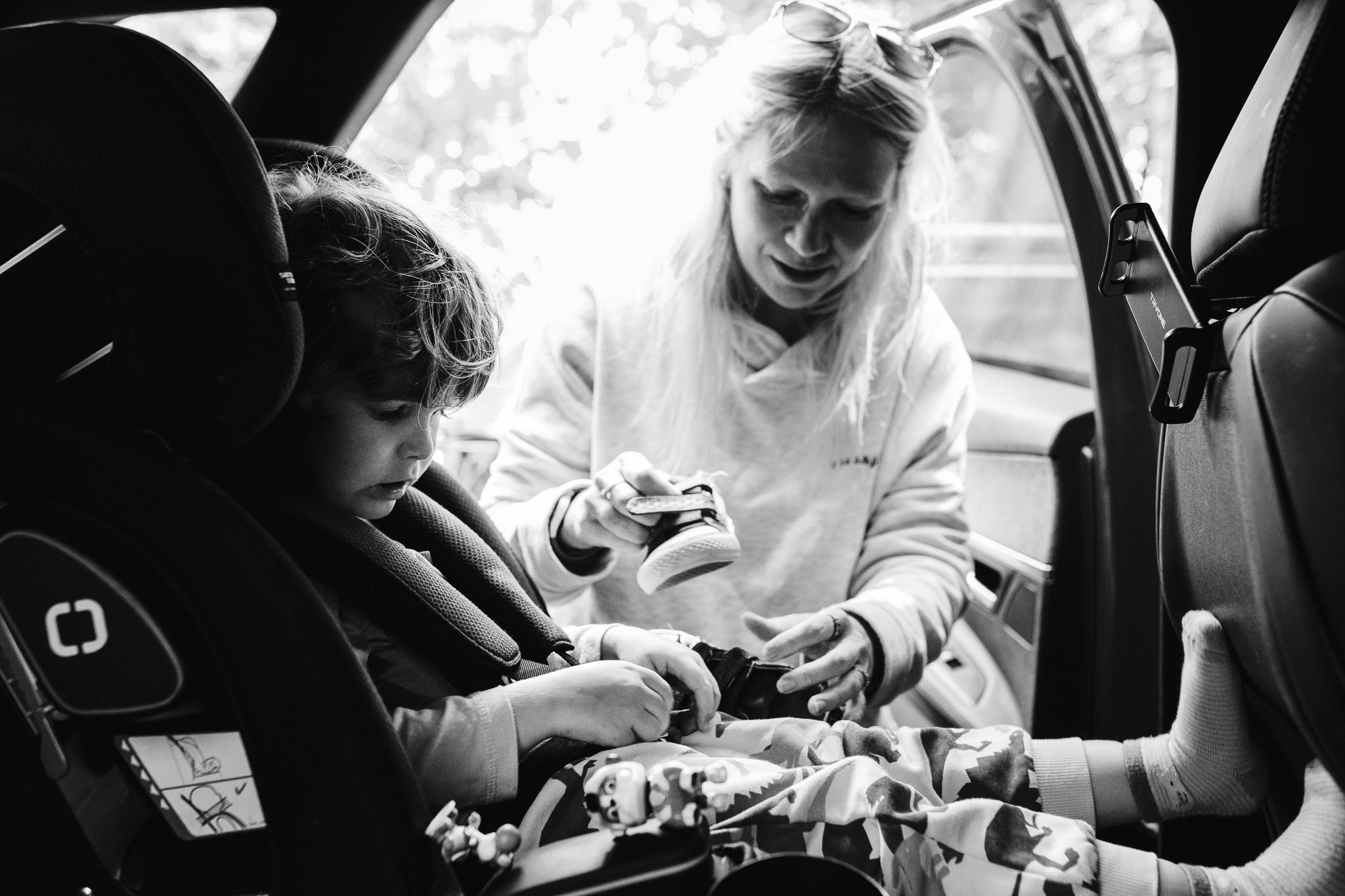 Mum is putting shoes onto her son in a car seat during a family photo session.