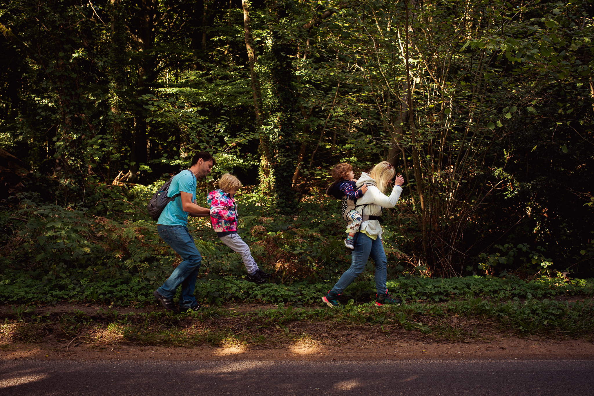 A family of four walking in a line along the road in a forest during a family photo session.