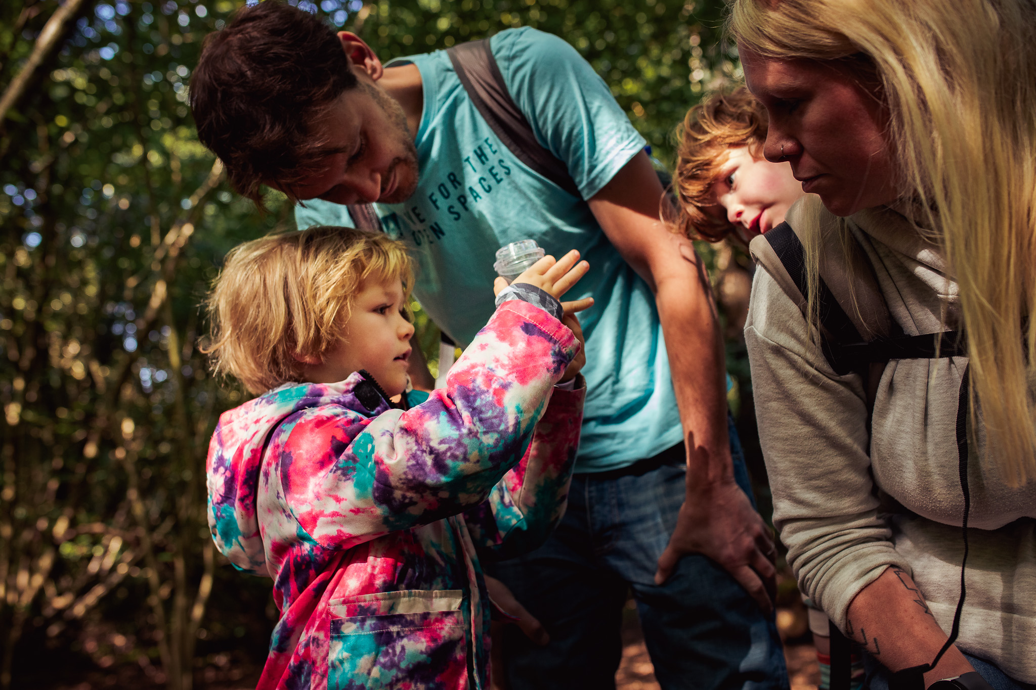 Family portrait of a young boy showing a jar with insects to his dad, mum, and young brother.