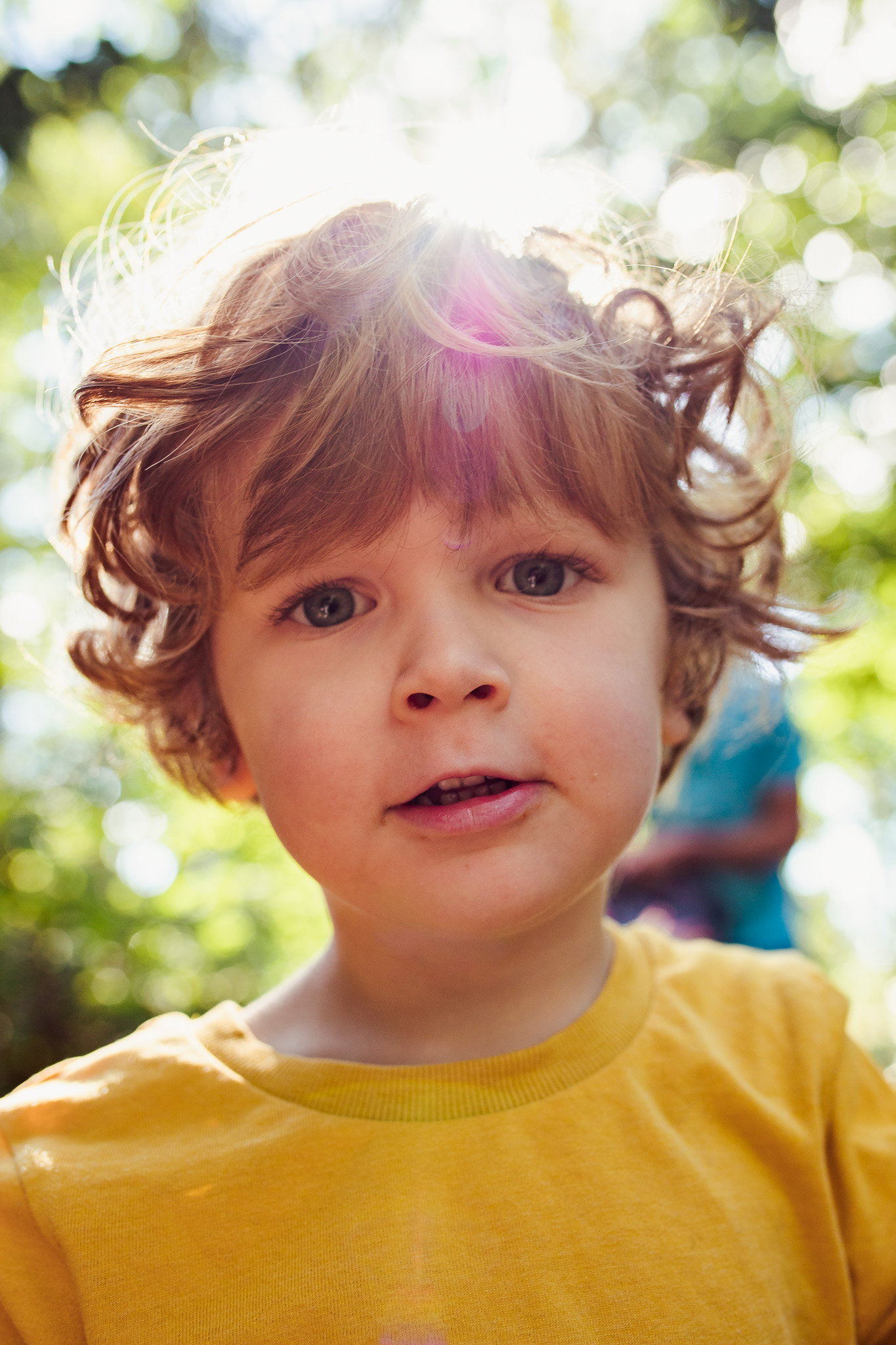 Leo wearing a yellow t-shirt with a sun flare behind his head and looking straight ahead during a family photo session.