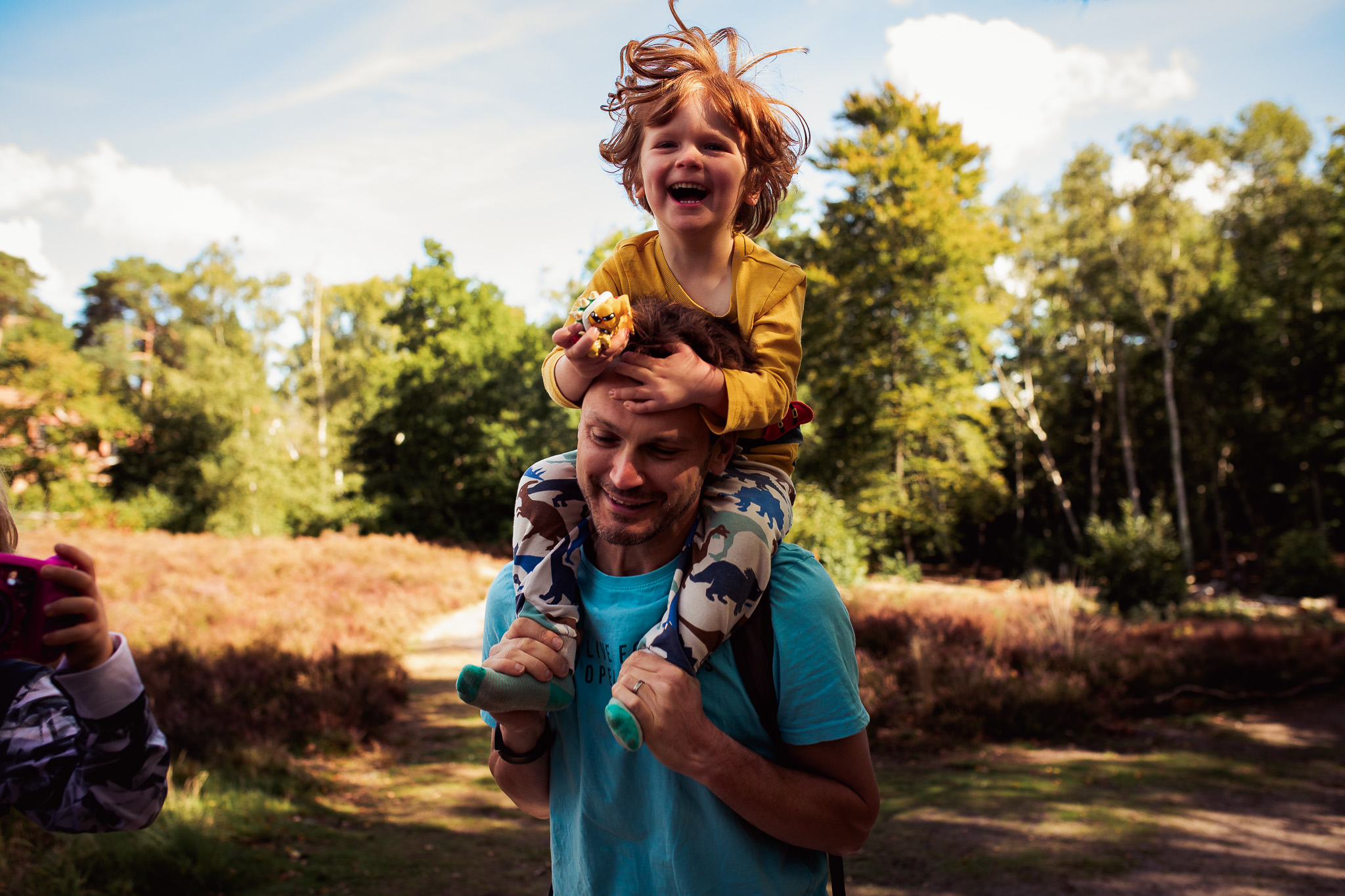 Dad bounces his laughing young son on his shoulders in a forest during a family photo session.