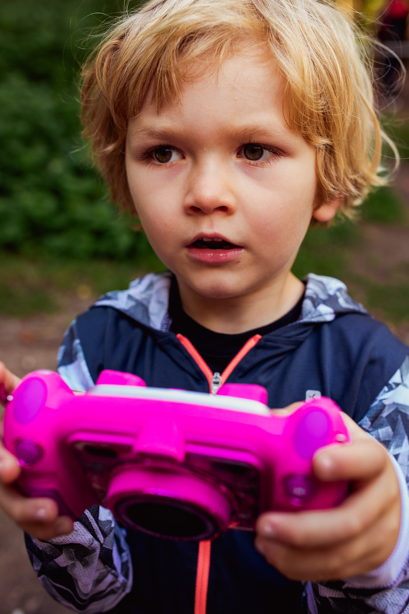 Kai holding a pink camera looking surprised during a family photo session.