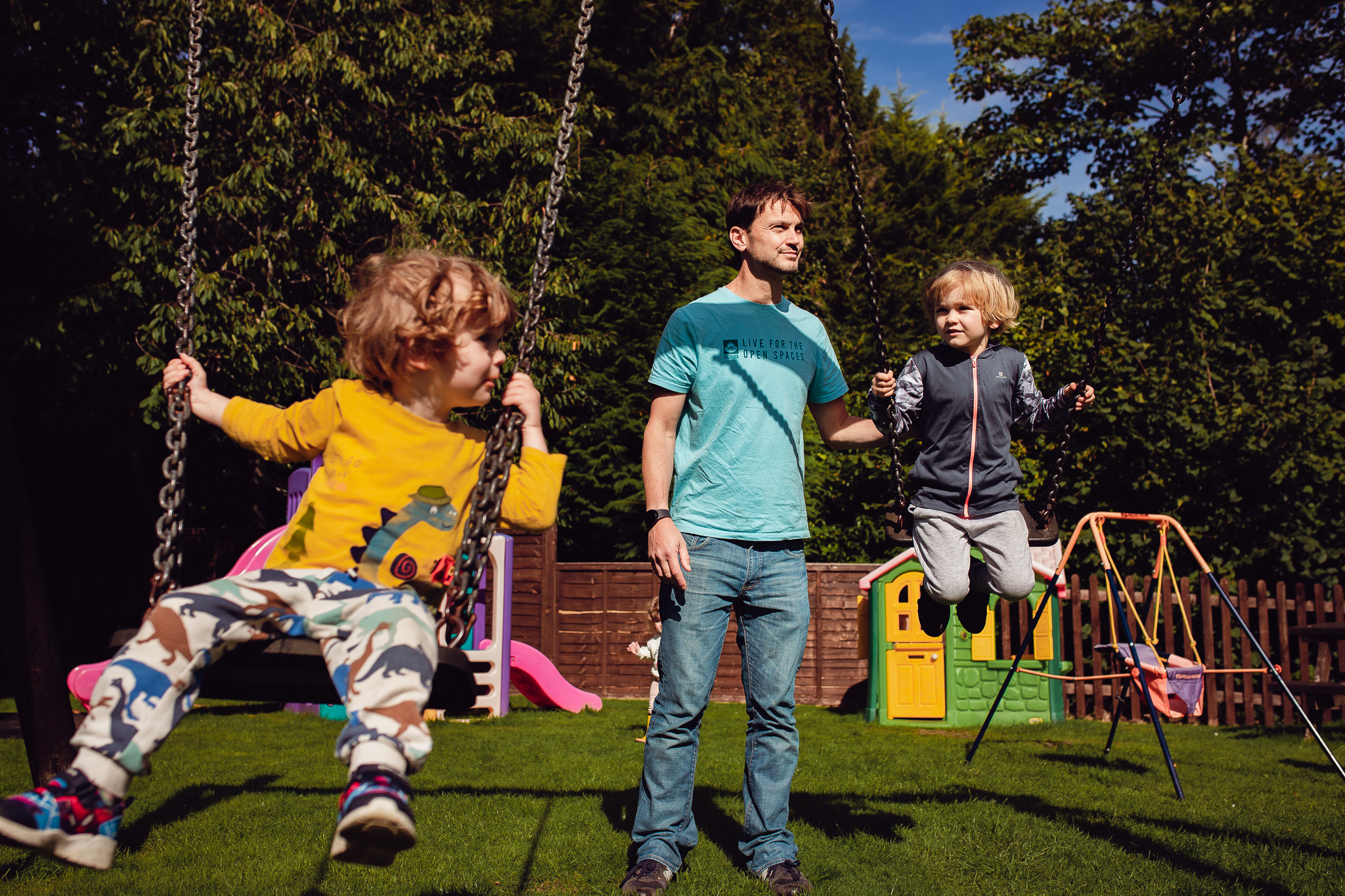 Two young boys being pushed on swings by their dad during a family photo session.