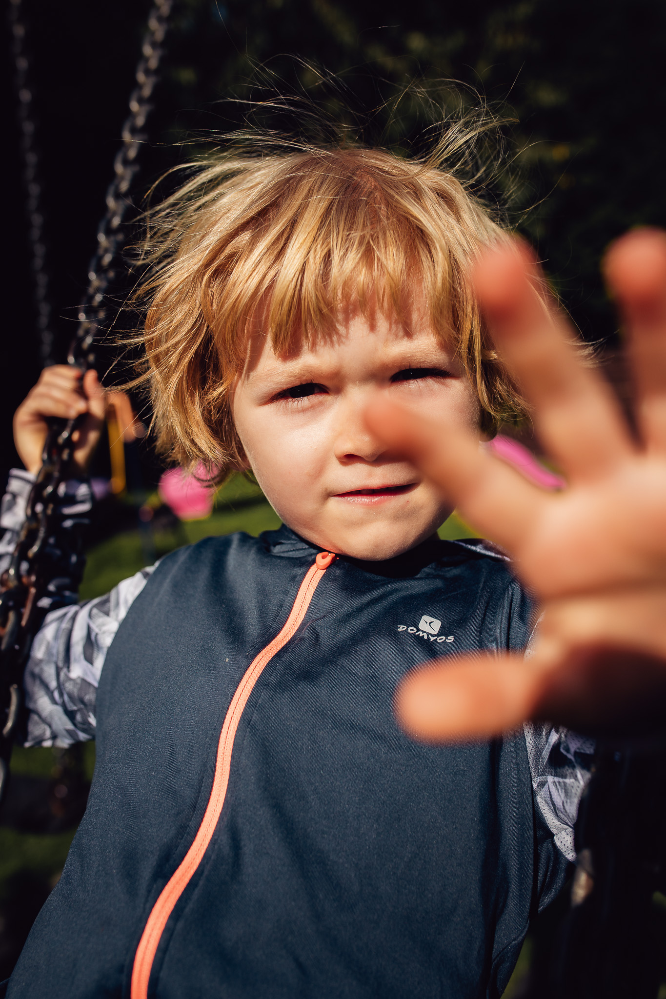 Young boy reaching out to cover his face on a swing during a family photo session.