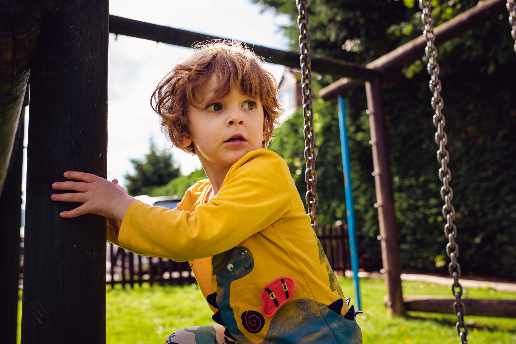 Leo in the playground wearing a yellow dinosaur t-shirt looking worried during a family photo session.