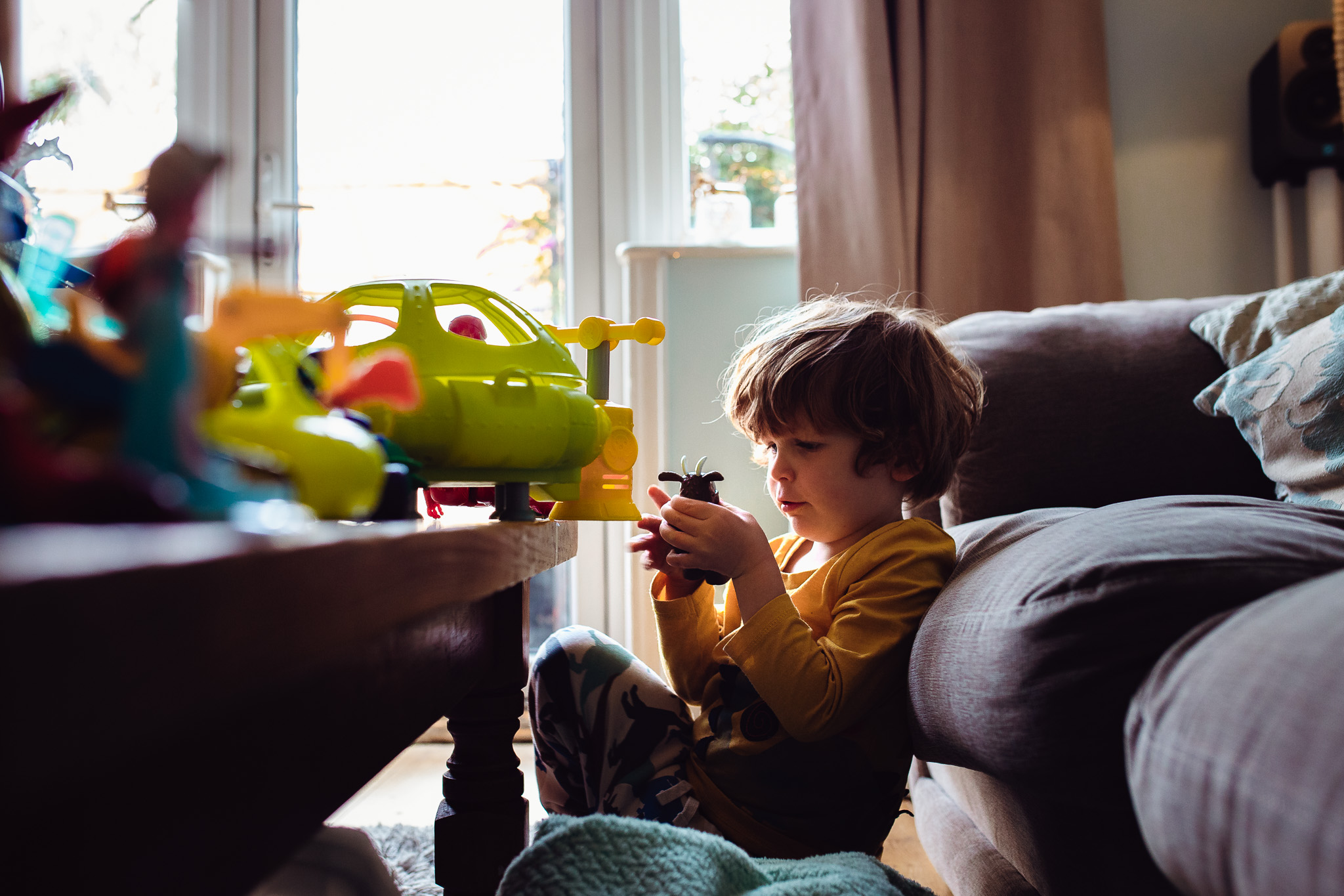 Leo sitting in between a sofa and coffee table playing with toys during a family photo session.